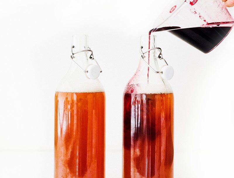 pouring blueberry kombucha ingredients into fermentation bottles