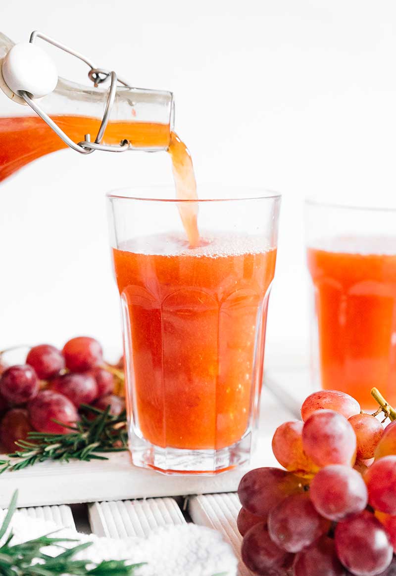 Pouring kombucha into a glass with grapes