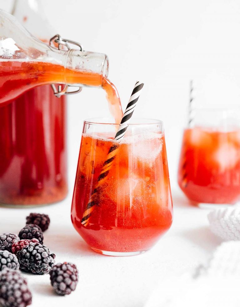 Pouring berry vanilla kombucha in a glass with a paper straw on white background