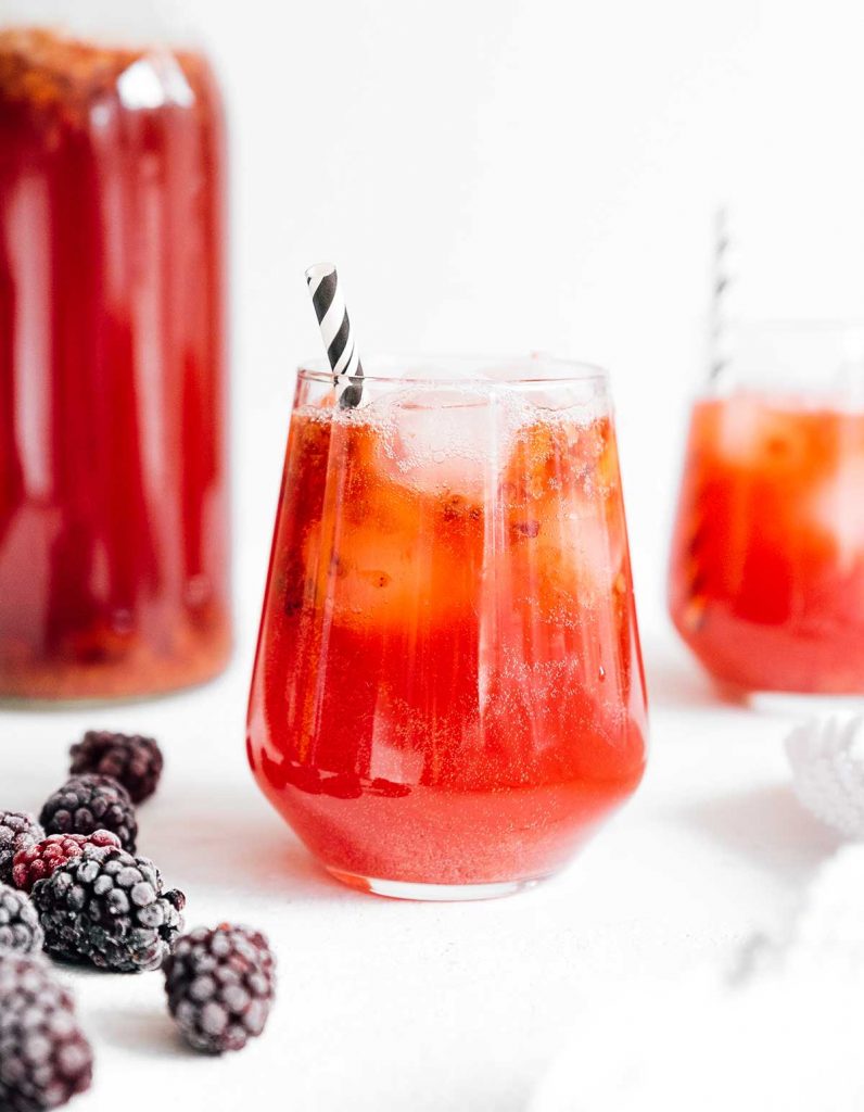 Blackberry kombucha in a glass with a paper straw on white background