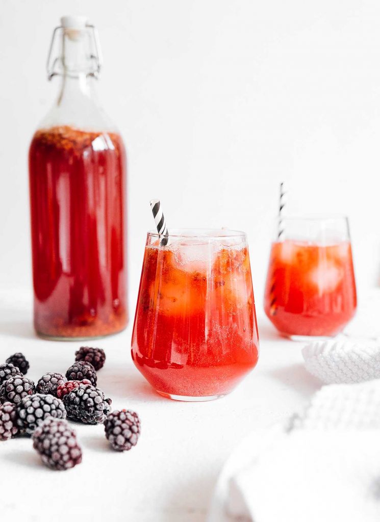 Blackberry kombucha in a glass with a paper straw on white background