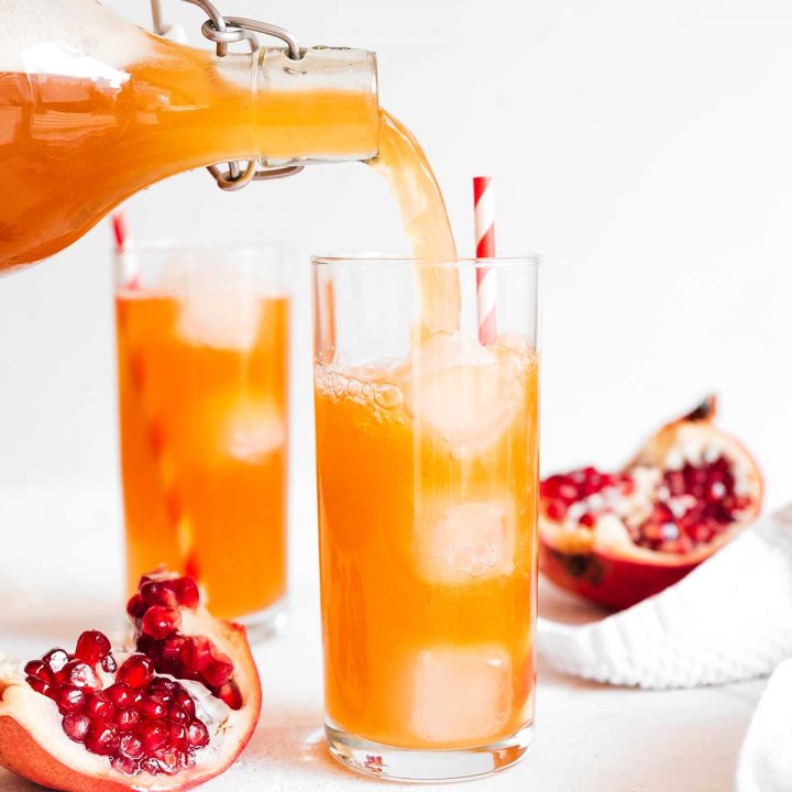 Pouring pomegranate kombucha in a glass on white background