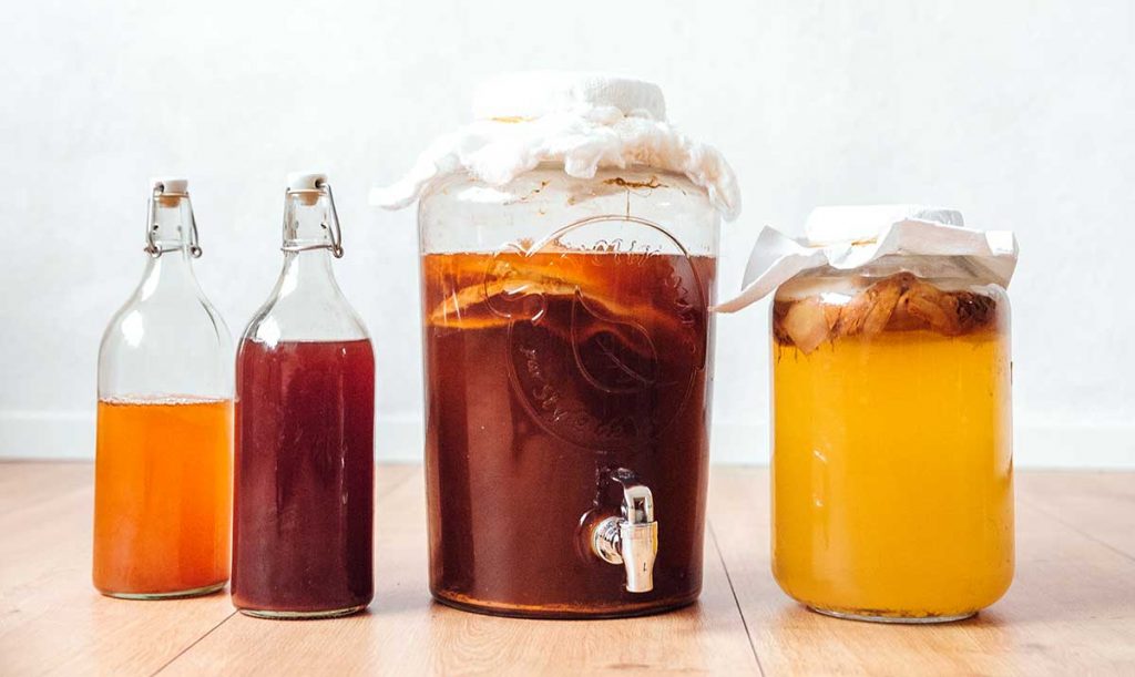 Bottles and jugs of kombucha on a wooden floor with white background