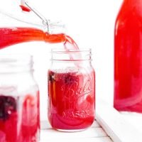 Pouring red cherry kombucha into a glass on a white background