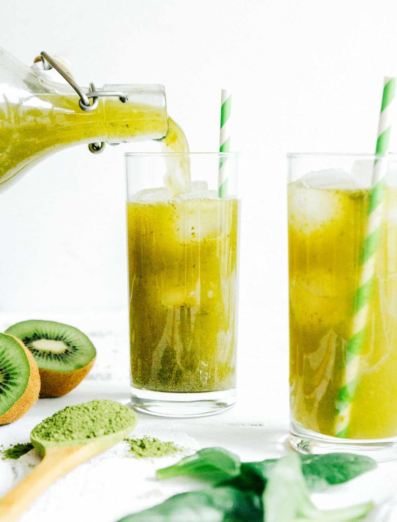 Green kombucha in a glass with a paper straw on a white background
