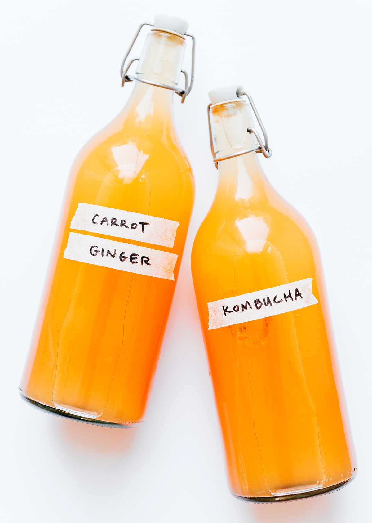 Carrot ginger kombucha in fermentation bottles on an orange background