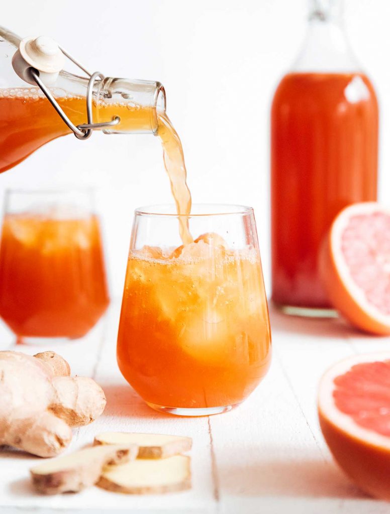 Pouring grapefruit kombucha into a glass on a white background