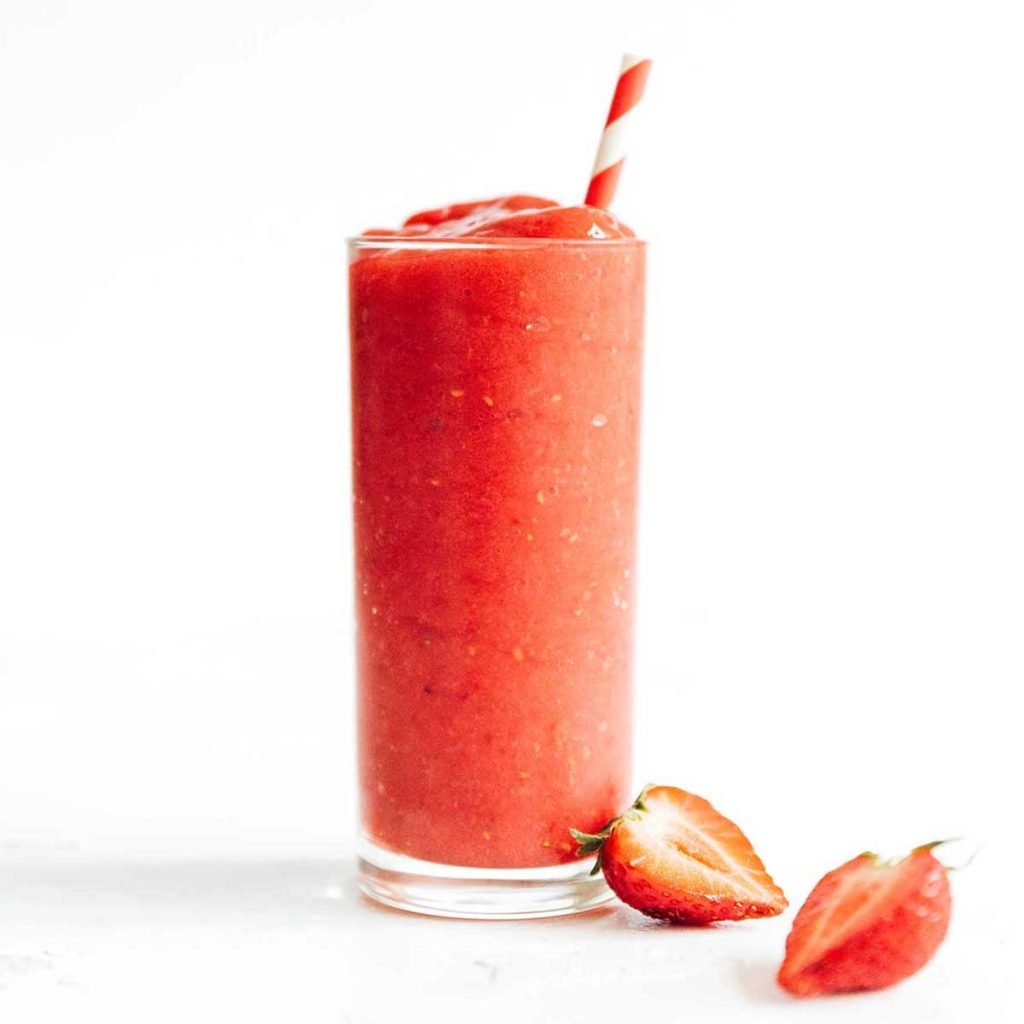 Red smoothie in a tall glass with striped straw and strawberries