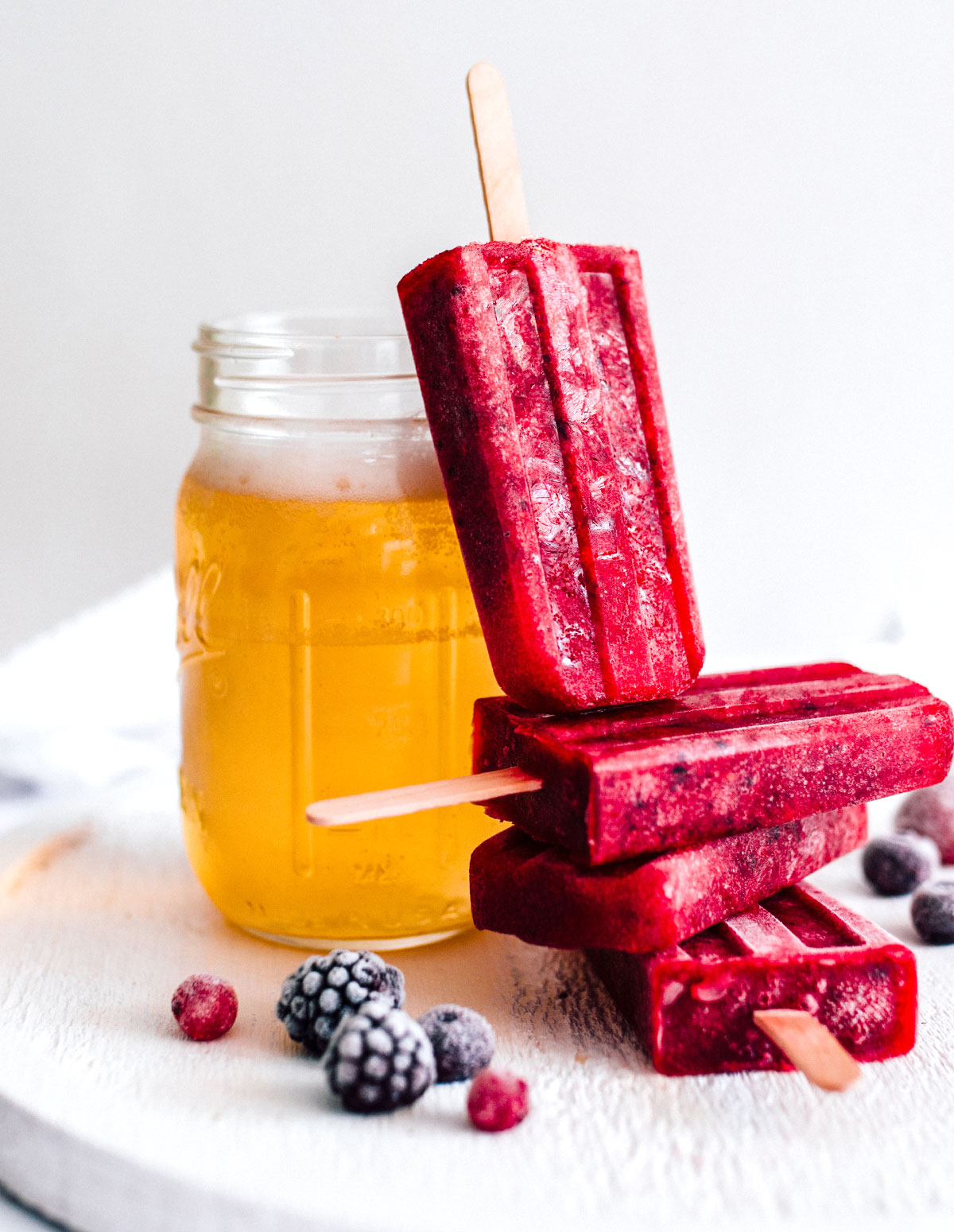 Red kombucha popsicles stacked next to a glass.