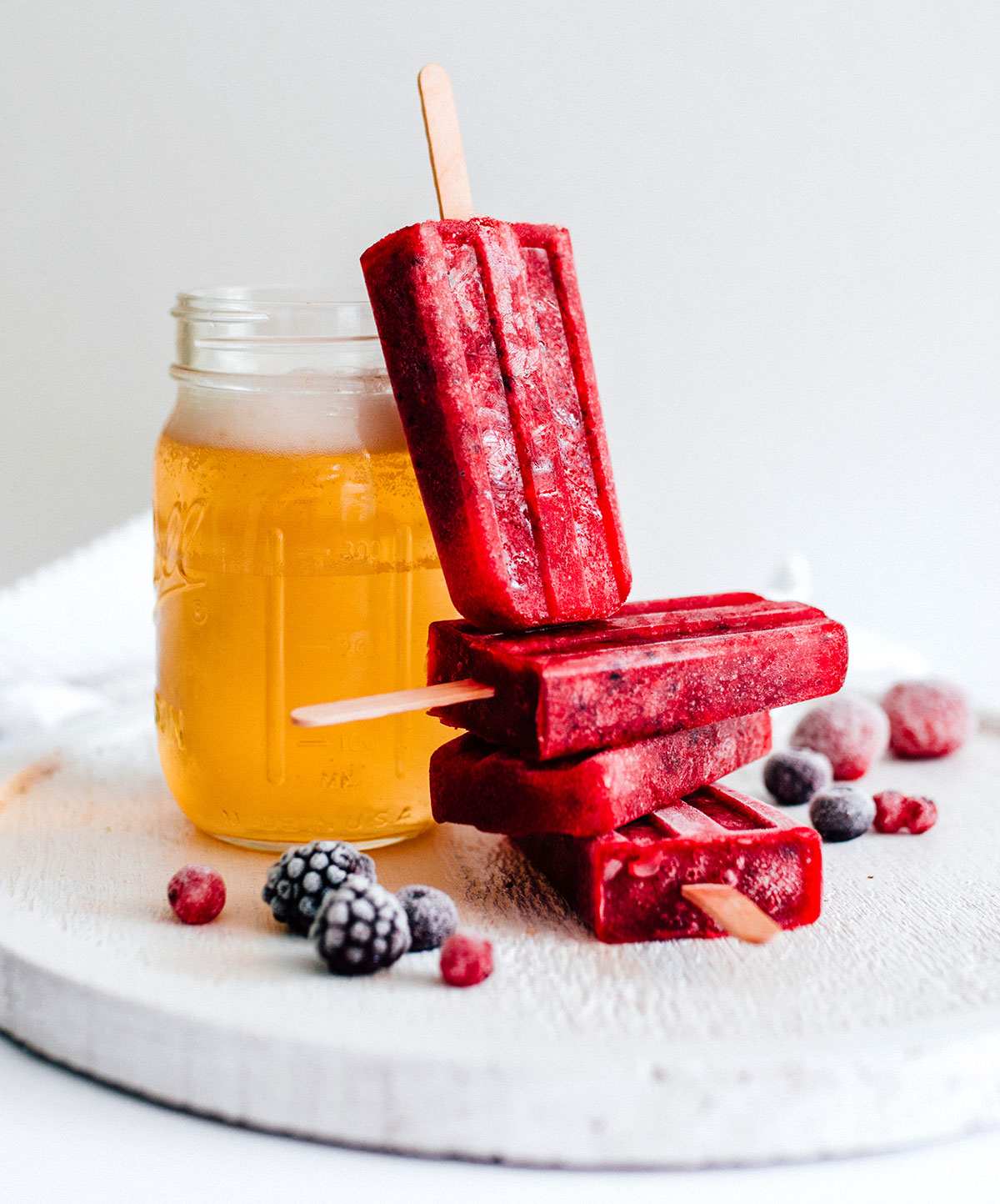 Red kombucha popsicles stacked next to a glass.